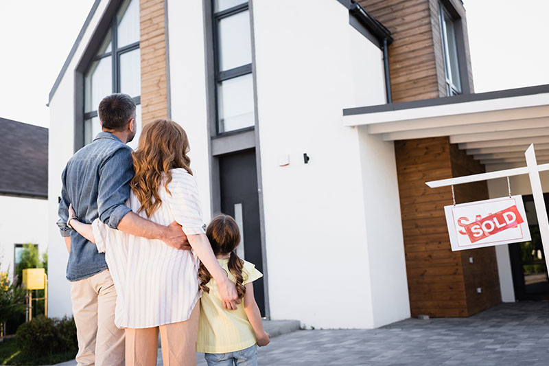 Familie steht vor einem Haus mit einem Schild auf dem Sold steht als Symbol zum Thema Haus verkaufen Schwalbach